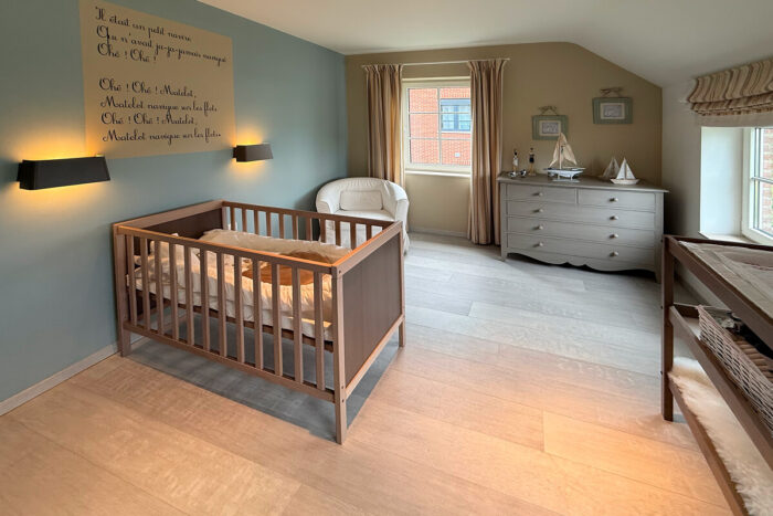 Een gezellige kinderkamer met een houten ledikant, bijpassende commode en commode. Zachte verlichting en een zeilbootdecor creëren een rustige sfeer - de perfecte inspiratie voor een huis kijkwoning Blavier Thorembais-Saint-Trond voor jouw droomgezinskamer.