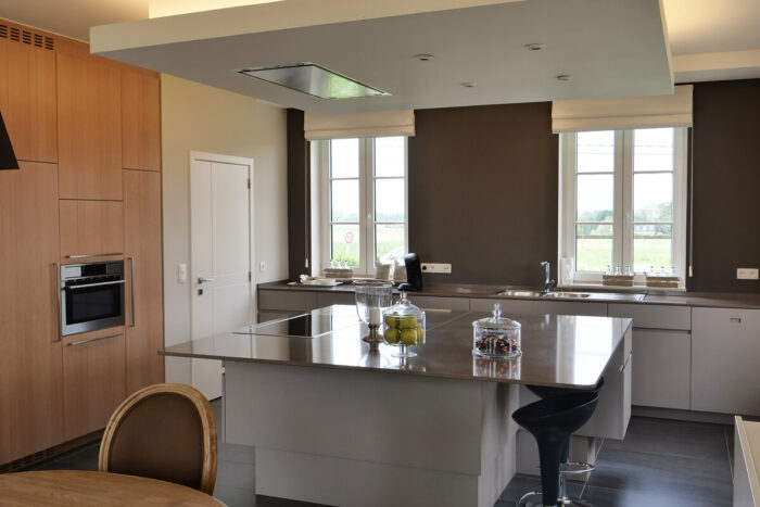 Moderne keuken met een groot kookeiland, barkrukken en strakke houten kasten. Geniet van natuurlijk licht en stijlvolle inbouwapparatuur - ontdek deze uitnodigende ruimte tijdens een bezoek kijkwoning Thorembais-Saint-Trond Blavier.