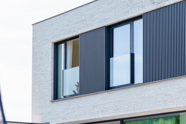 Une façade de bâtiment moderne avec de grandes fenêtres à persiennes verticales rayées. L'extérieur est fait de briques blanches, créant un design élégant et contemporain.