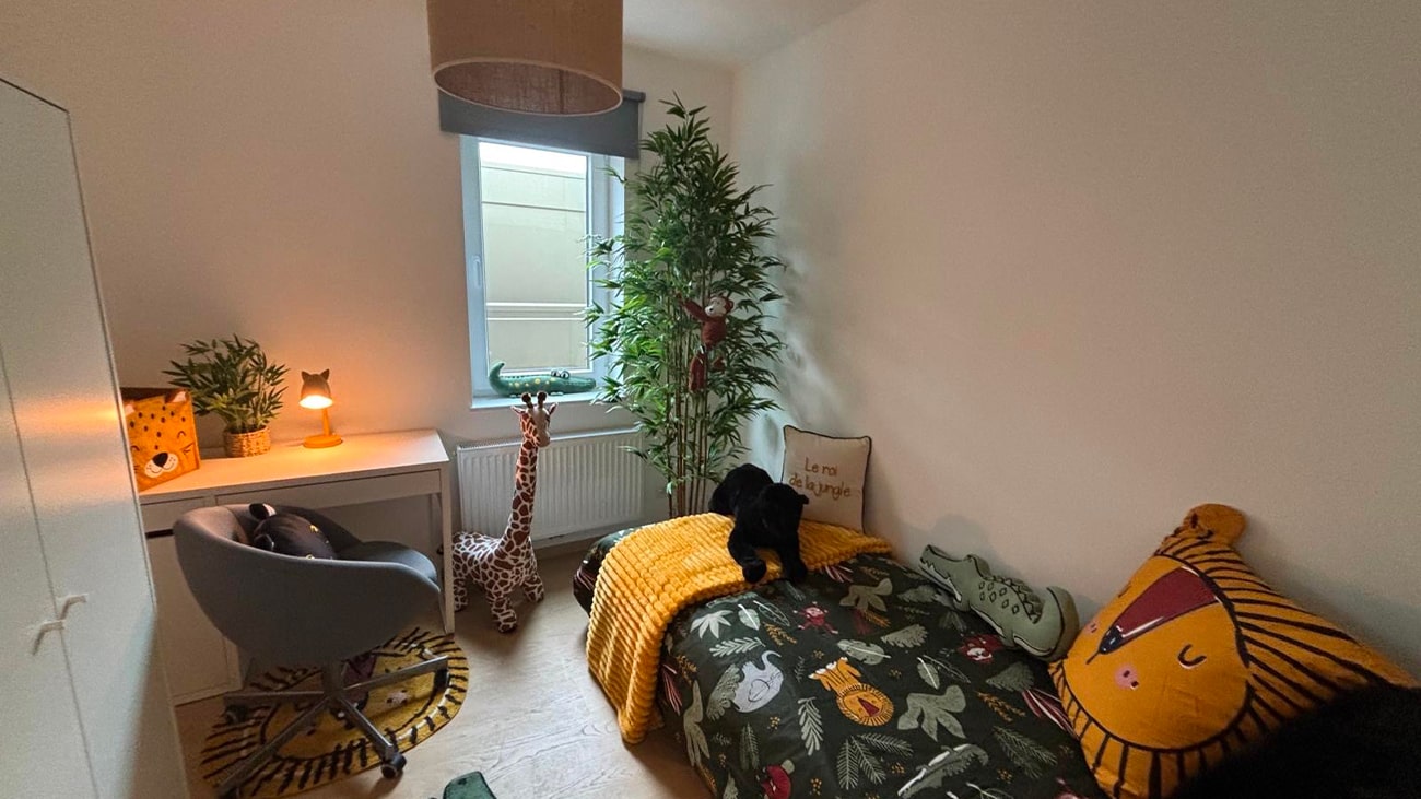 Une chambre denfant douillette sur le thème de la jungle vous attend dans ce charmant appartement à vendre à Jambes. Doté dun lit simple avec une literie à imprimé animalier, dun jouet girafe et dune peluche panda, il offre fantaisie et fonctionnalité. Une grande plante et un bureau côté fenêtre complètent cet espace serein.