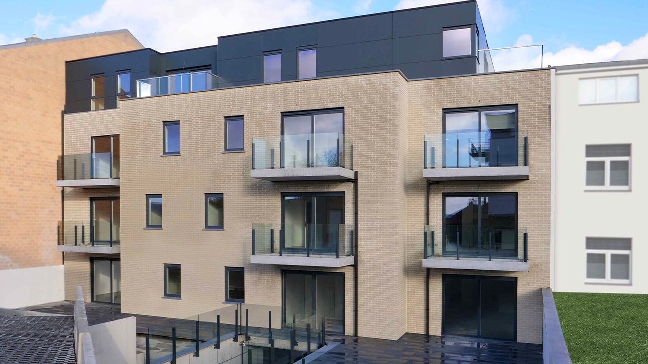 Appartement moderne à vendre à Jambes, ce bâtiment présente une façade en briques beiges, de grands balcons en verre et un toit plat. La structure possède plusieurs étages avec des détails sombres, se détachant sur un ciel bleu clair, flanquée par dautres bâtiments visibles sur les côtés.
