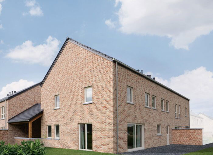 Une maison moderne en brique avec un toit à pignon, dotée de plusieurs fenêtres et dune porte coulissante en verre. Le bâtiment est entouré dune pelouse et de quelques plantes, sur fond de ciel bleu clair parsemé de nuages.