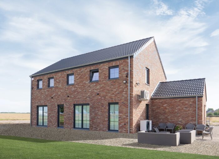 Een modern bakstenen huis van twee verdiepingen met grote ramen en een grijs pannendak, met een patio met zitplaatsen, op een ondergrond van grind naast een groen gazon onder een blauwe hemel.