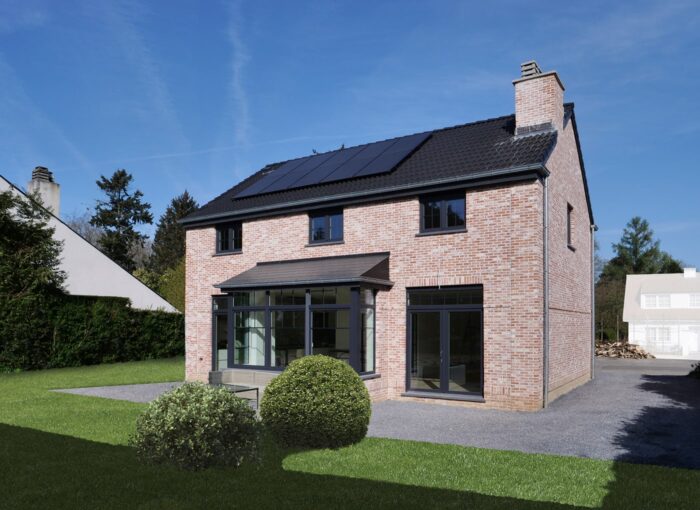 Une maison moderne en briques à deux étages avec des fenêtres à cadre noir, des panneaux solaires sur le toit et une extension de véranda en verre, entourée d'une pelouse verte et d'arbustes paysagers sous un ciel bleu clair.