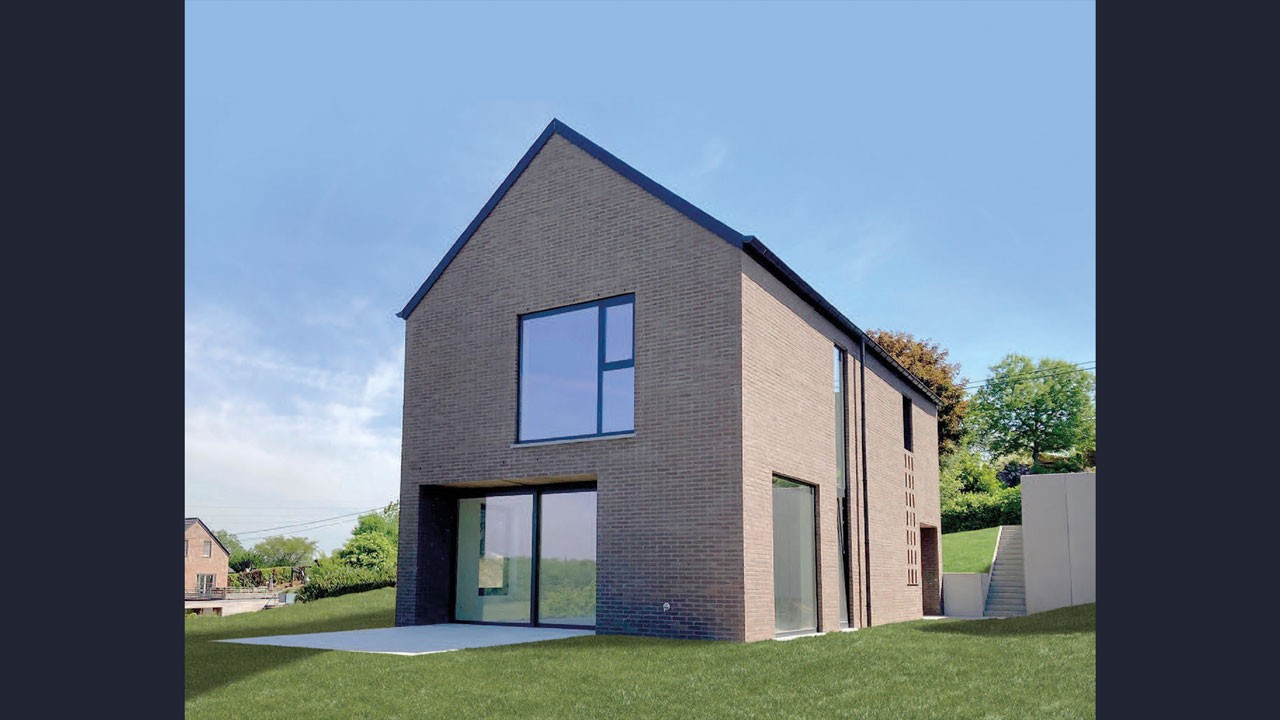 Une maison moderne à deux étages, avec sa façade en briques, ses grandes fenêtres et son toit en pente, se dresse sur une pelouse verdoyante sous un ciel bleu azur. On aperçoit une terrasse en béton à l'arrière-plan, avec des arbres et d'autres maisons en arrière-plan.