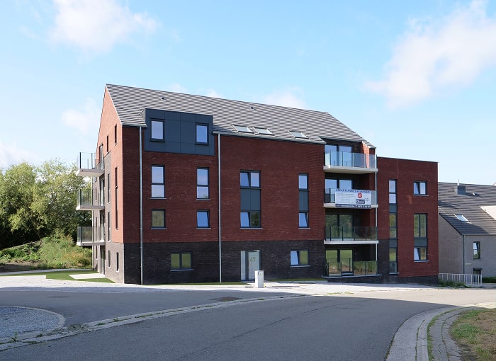 Un immeuble moderne de trois étages avec des briques rouges et sombres à l'extérieur, de nombreuses fenêtres, des balcons et un panneau 
