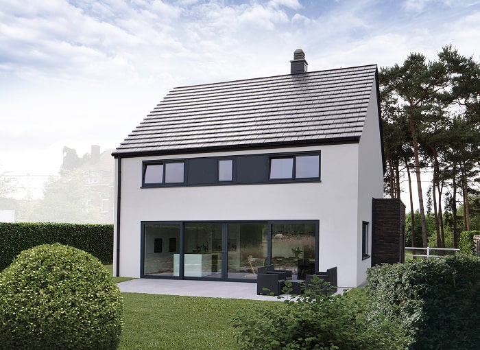 Maison moderne de deux étages avec des murs blancs, des fenêtres à cadre sombre et un toit en tuiles grises, entourée de buissons et d'arbres verts, avec un patio et des meubles d'extérieur dans l'arrière-cour.