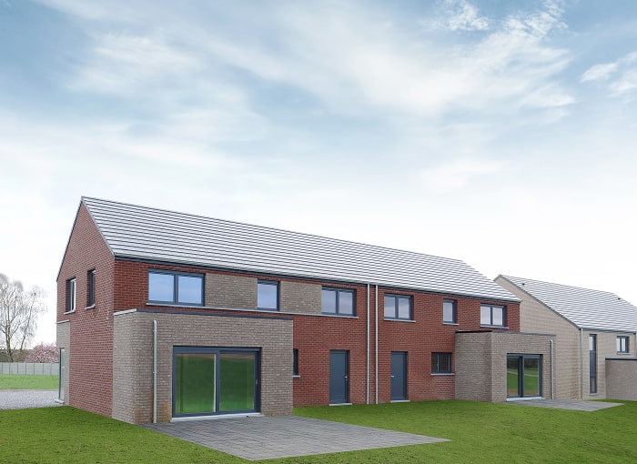 Een rij moderne, bakstenen huizen van twee verdiepingen met grote ramen en glazen schuifdeuren, op een grasveld onder een gedeeltelijk bewolkte blauwe hemel.