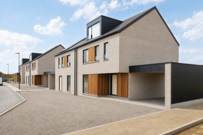 Une rangée de maisons modernes en briques à deux étages, agrémentées de détails en bois et dotées de grandes fenêtres, alignées le long d'une rue propre et calme, sous un ciel partiellement nuageux.