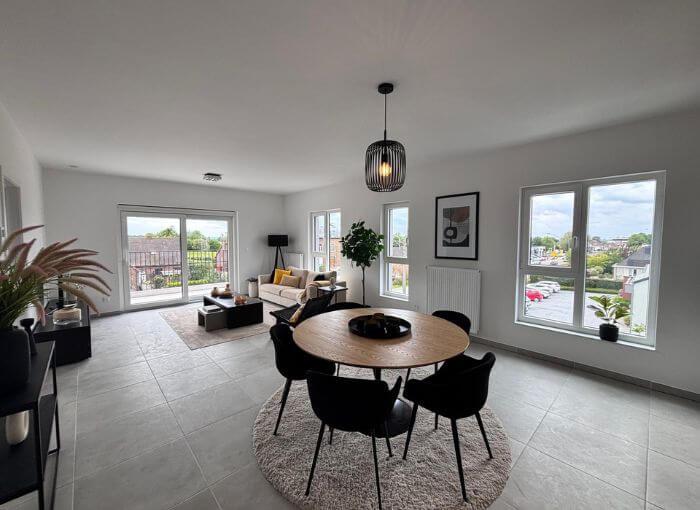 Salon-salle à manger moderne et lumineux, doté de grandes fenêtres, d'une table ronde entourée de quatre chaises noires, d'un canapé beige, de plantes et d'une décoration minimaliste, avec un balcon et une vue sur la ville.